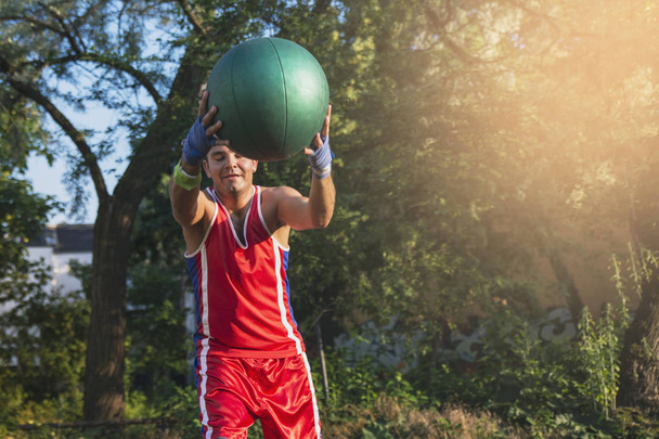 Young athlete performs sports exercises with a ball outdoors - Valokuva, kuva