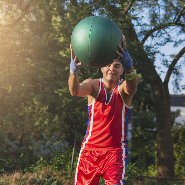 Молодий спортсмен виконує спортивні вправи з м'ячем на відкритому повітрі
 - Фото, зображення