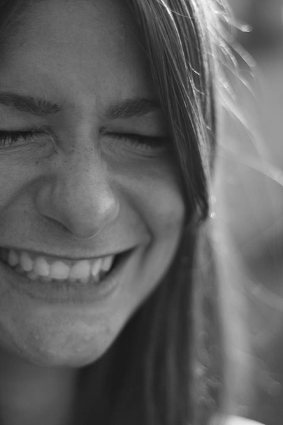 Young woman portrait in black and white. Smiling with tight closed teeth and eyes.  - Φωτογραφία, εικόνα