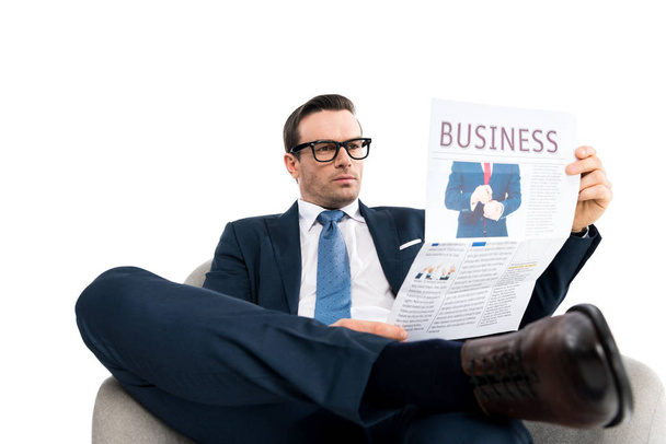 confiado hombre de negocios de mediana edad en anteojos sentado en sillón y leyendo periódico aislado en blanco
 - Foto, Imagen