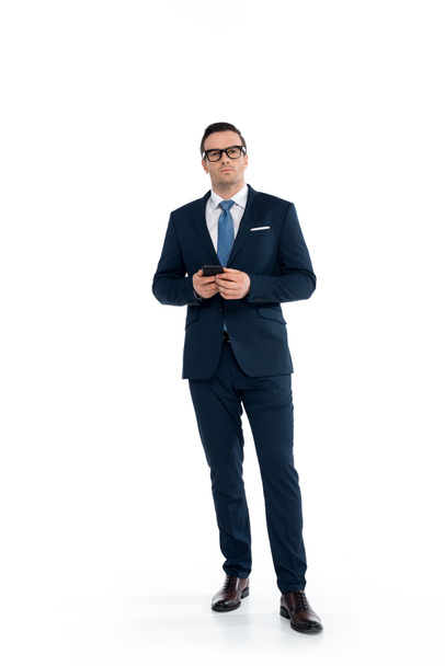 full length view of confident buisnessman in eyeglasses holding smartphone and looking at camera isolated on white - Foto, immagini
