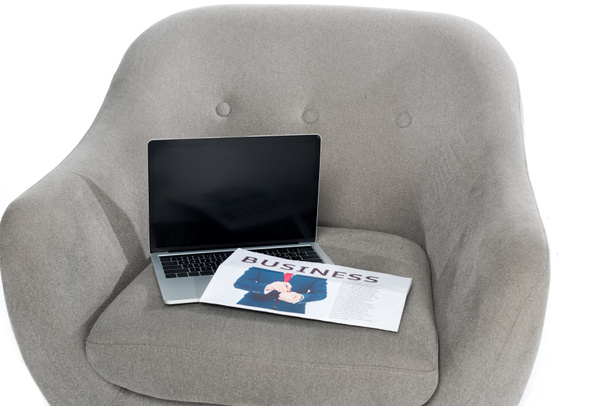 laptop with blank screen and business newspaper on grey armchair - Foto, afbeelding