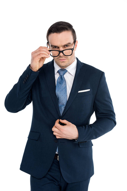 handsome businessman adjusting eyeglasses and looking at camera isolated on white - Photo, Image