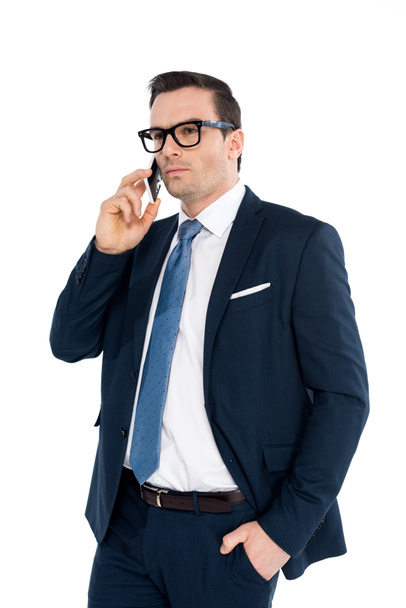 handsome businessman in formal wear talking by smartphone and looking away isolated on white  - Photo, Image