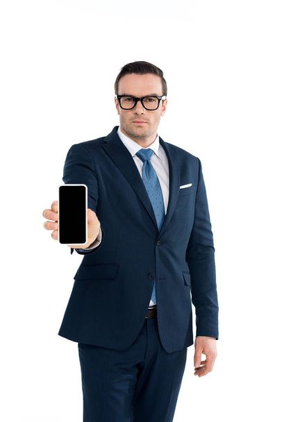 handsme businessman in eyeglasses holding smartphone with blank screen and looking at camera isolated on white - Photo, Image
