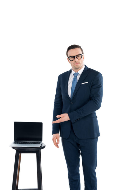 middle aged buisnessman in eyeglasses pointing at laptop with blank screen and looking at camera isolated on white - Foto, Imagen