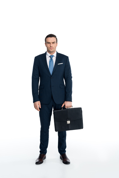 full length view of serious middle aged businessman holding briefcase and looking at camera on white - Φωτογραφία, εικόνα