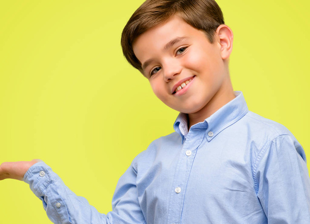 Όμορφος νήπιο παιδί με πράσινα μάτια κρατώντας κάτι στο άδειο χέρι πάνω από το κίτρινο φόντο - Φωτογραφία, εικόνα