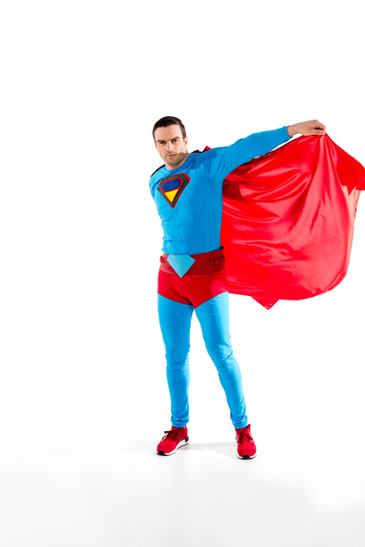 handsome man in superhero costume and cloak looking at camera isolated on white - Fotó, kép