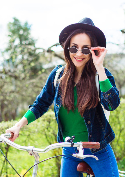 jonge vrouw in zwarte hoed poseren op fiets - Foto, afbeelding
