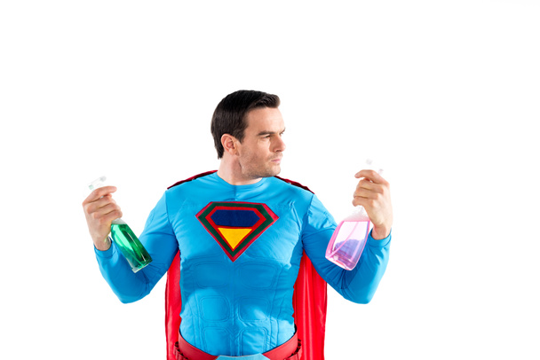 handsome superhero holding plastic spray bottles with cleaning liquid isolated on white  - Photo, Image
