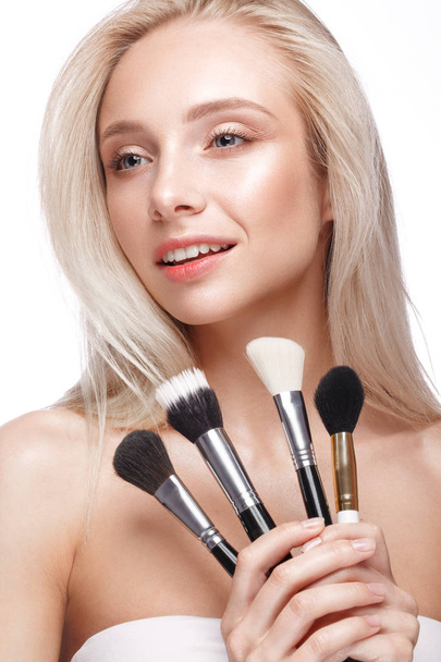 Beautiful young girl with a light natural make-up,brushes for cosmetics and nude manicure. Beauty face. Picture taken in the studio on a white background. - Фото, изображение