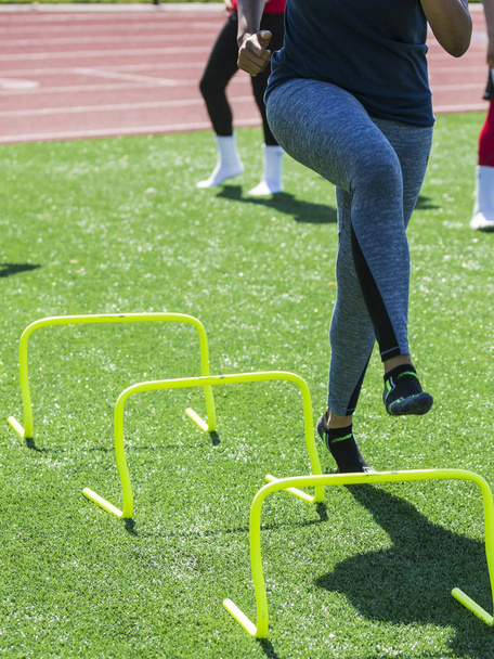A runner is performing speed drills ovr yellow mini banana hurdles with no shoes on during trak and field practice. - Photo, Image