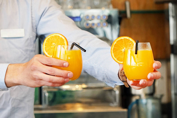 De barman geeft twee glazen van jus d'orange aan de cliënt van het restaurant van het hotel. De ober brengt het betalingsbevel twee jus d'orange aan de cliënt van de bar van het hotel. Het begrip dienst. - Foto, afbeelding