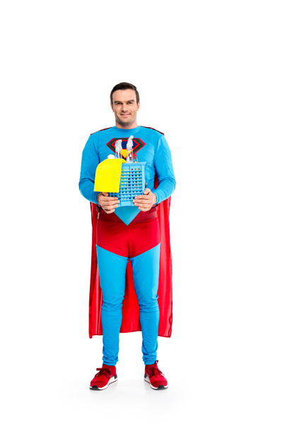 handsome male superhero holding cleaning supplies and smiling at camera isolated on white - Photo, Image