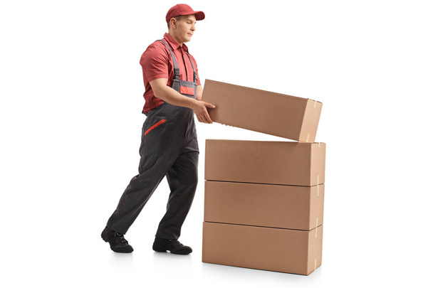 Full length profile shot of a mover placing a package on top of a stack isolated on white background - Zdjęcie, obraz