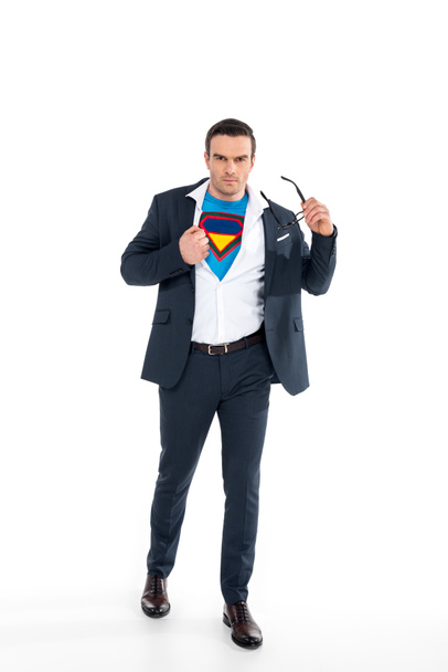 Selbstbewusster Geschäftsmann im Superheldenkostüm unter Anzug, Brille abnehmend und Kamera isoliert auf Weiß blickend - Foto, Bild