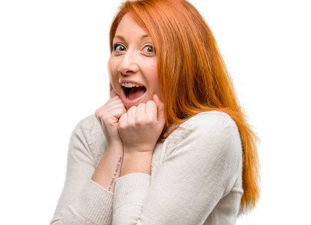 Όμορφη νεαρή κοκκινομάλλα γυναίκα ευτυχισμένη και έκπληκτος επευφημίες εκφράζοντας wow χειρονομία απομονωθεί σε λευκό φόντο - Φωτογραφία, εικόνα