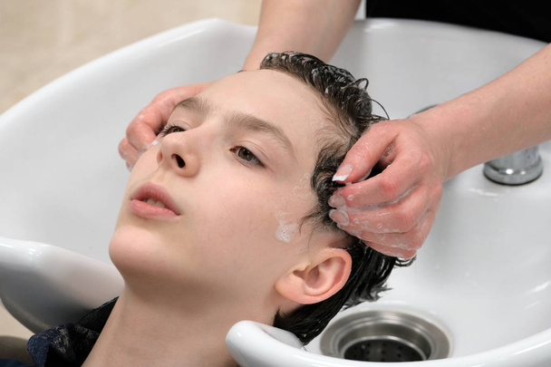 Les mains féminines du coiffeur savonnent les cheveux du gars avant la coupe de cheveux. Une femme lave la tête d'un jeune homme dans un salon de beauté
. - Photo, image