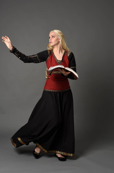 portrait complet de jolie dame blonde portant une robe médiévale fantaisie rouge et noire. pose debout sur fond gris
. - Photo, image