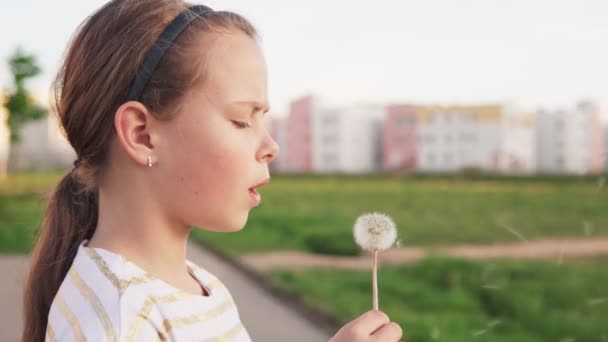Cute little girl blowing on dandelion on city lawn - Footage, Video