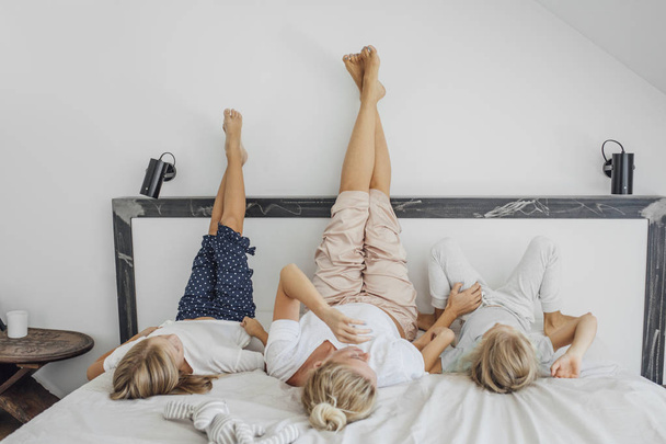Mother and her two cute daughters lying on cozy king-size bed upside-down. - Foto, Imagem