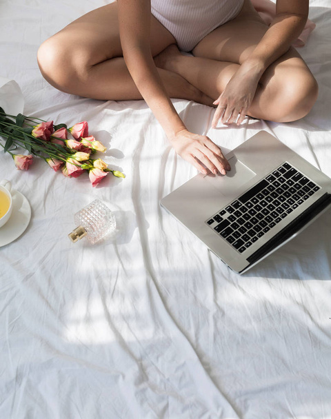 Cropped unrecognisable woman sitting on her bed in the morning and typing on her laptop. - Foto, Imagem