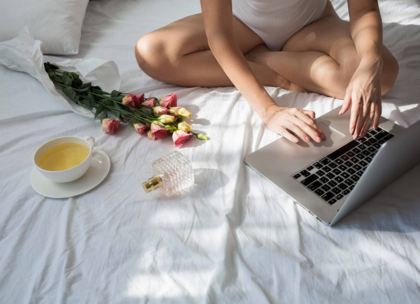 Cropped unrecognisable woman sitting on her bed in the morning and typing on her laptop. - Foto, Imagem
