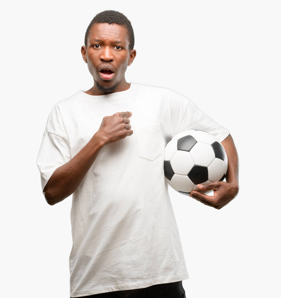 Africain noir tenant ballon de football heureux et surpris acclamations exprimant wow geste, pointant du doigt
 - Photo, image