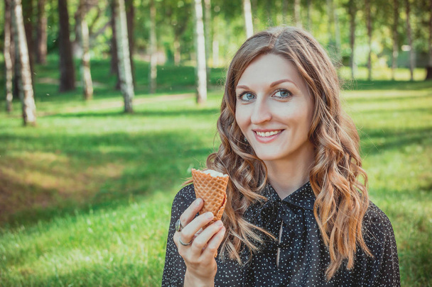 young curly wooman holding an ice cream cone and cheerful smiling - Фото, изображение
