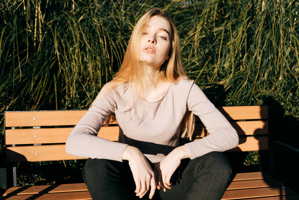 attractive young blonde girl sits on a bench outdoors in the sun, posing - Valokuva, kuva