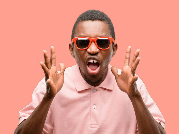 African black man wearing sunglasses stressful keeping hands on head, terrified in panic, shouting - 写真・画像