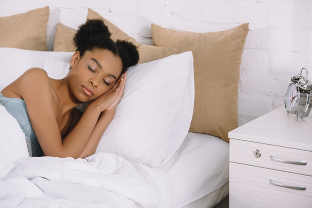 beautiful african american girl sleeping on bed with alarm clock near - Foto, Bild