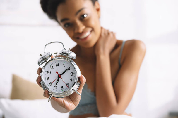 selective focus of afro girl showing alarm clock in morning - Fotó, kép