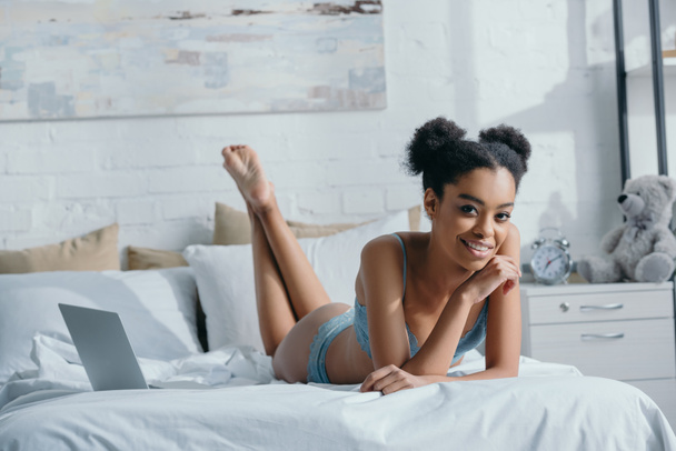 Szczęśliwa dziewczyna Afryki amerykański w bieliźnie leżąc na łóżku z laptopa - Zdjęcie, obraz