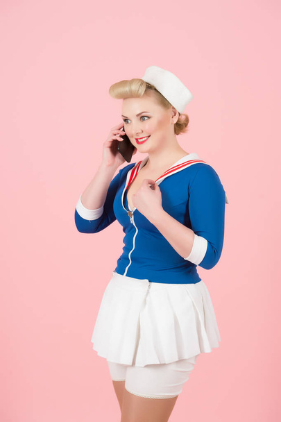 Anime style woman talks over smart-phone on rose background. Attractive young sailor girl with blonde curl and pin-up makeup communicate via cellular - Foto, Bild