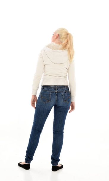портрет блондинки в білому светрі і джинсах. стояча поза на білому фоні студії
 - Фото, зображення
