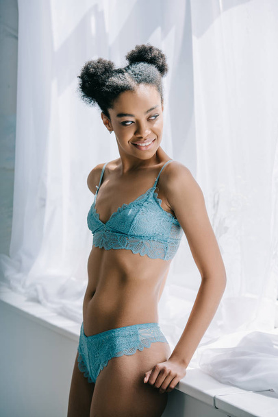 attractive young african american woman in blue lingerie posing near window  - Foto, Bild