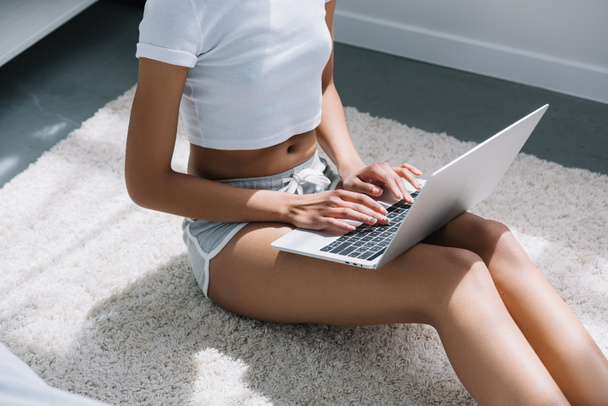 vista recortada de chica afroamericana escribiendo en el ordenador portátil blanco sentado en el suelo
  - Foto, Imagen