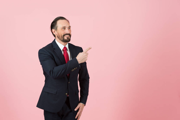 Handsome middle age man in suit and red tie pointing away side with his finger with pink rose background - Fotografie, Obrázek