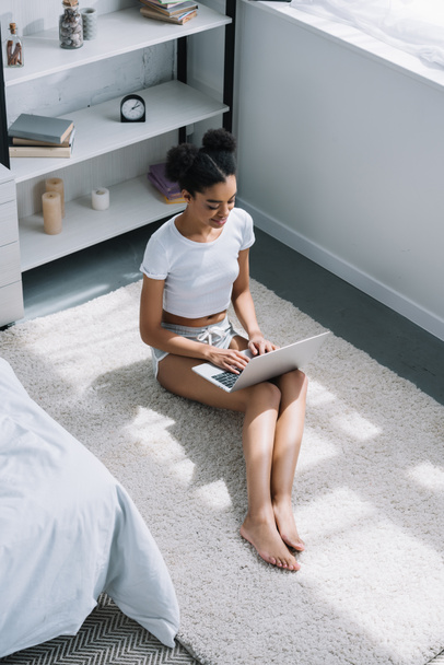 high angle view of african american girl using laptop white sitting on floor in bedroom - Fotografie, Obrázek