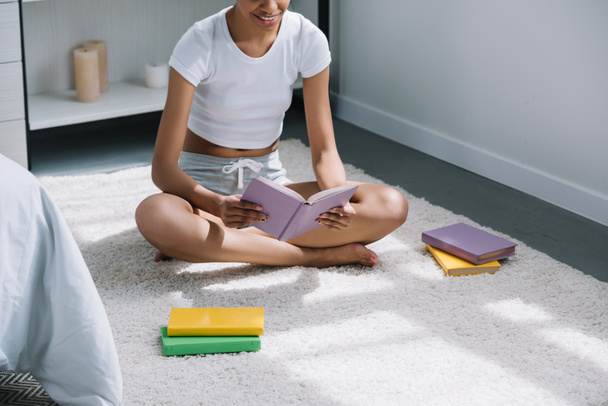 περικοπεί θέα Αφρικανικός Αμερικανός φοιτητής διαβάζοντας το βιβλίο στο πάτωμα στην κρεβατοκάμαρα - Φωτογραφία, εικόνα