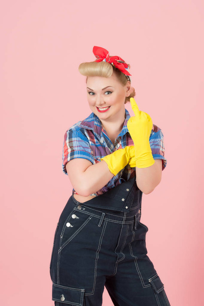 Blonde Housewife in pin-up style showing middle finger in yellow gloves. blonde curls girl with red headscurf and cleaning gloves is going make cleaning. young pretty woman cleaner against dust. - Foto, immagini