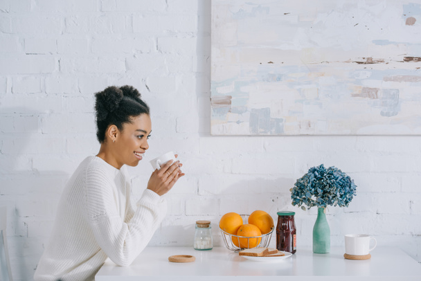 vista lateral da jovem mulher feliz com xícara de café da manhã em casa
 - Foto, Imagem