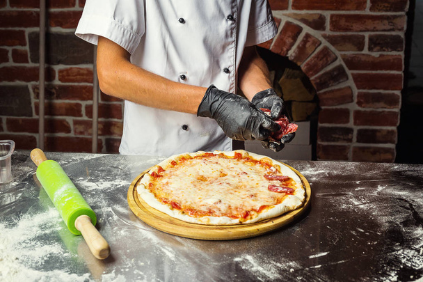 Cook (Chef) making delicious pizza at the restaurant, close-up - Photo, Image