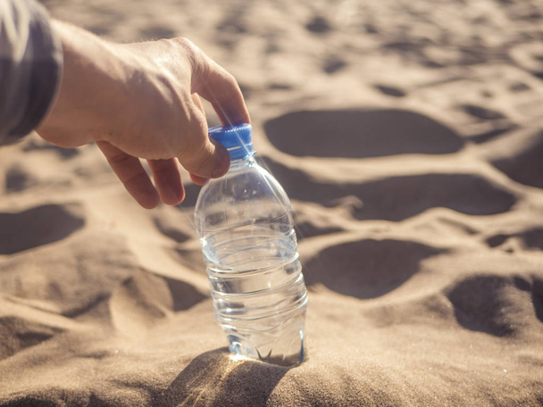 személy megnyitja az ivóvíz palackozott víz, a homok, a tenger partján - Fotó, kép