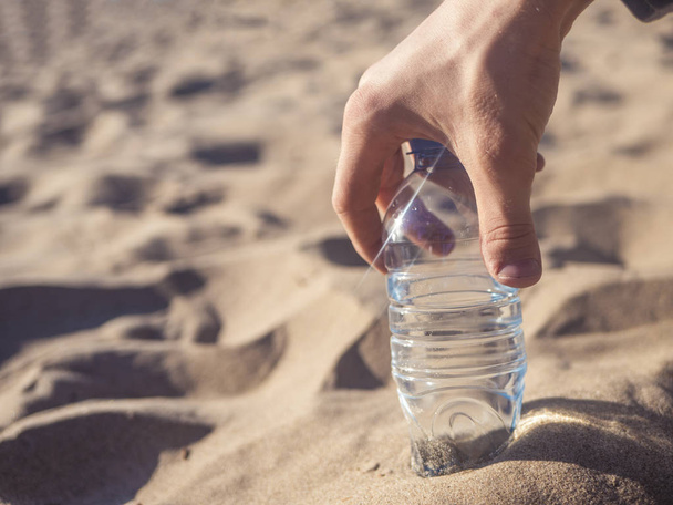 garrafa mão segurando com água na praia do mar arenoso
 - Foto, Imagem