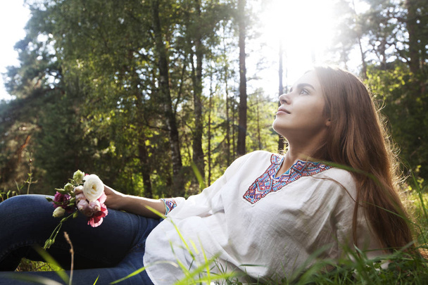 Relaxing young woman with bouquet of pink flowers on the forest clearing - Foto, Bild