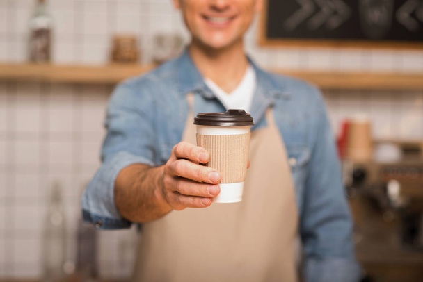 cropped shot of waiter holding coffee to go in paper cup with blurred background - Zdjęcie, obraz