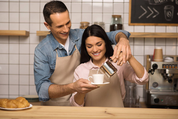 smiling young couple in aprons preparing coffee together in cafe - Photo, Image
